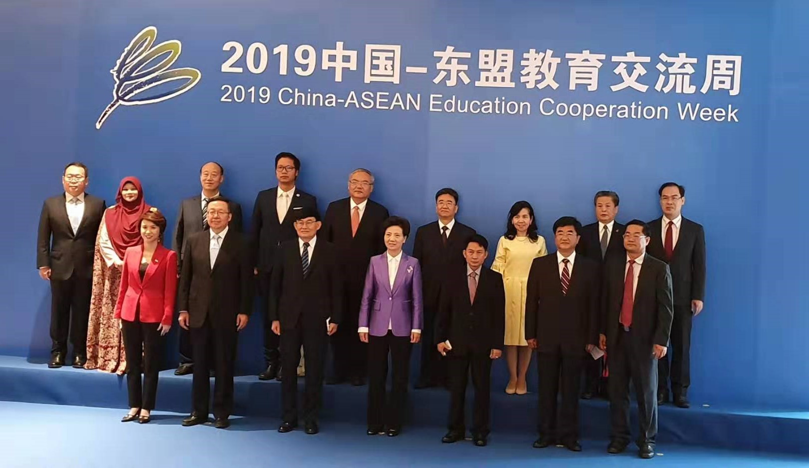 Group of formally dressed people posed against a blue backdrop.